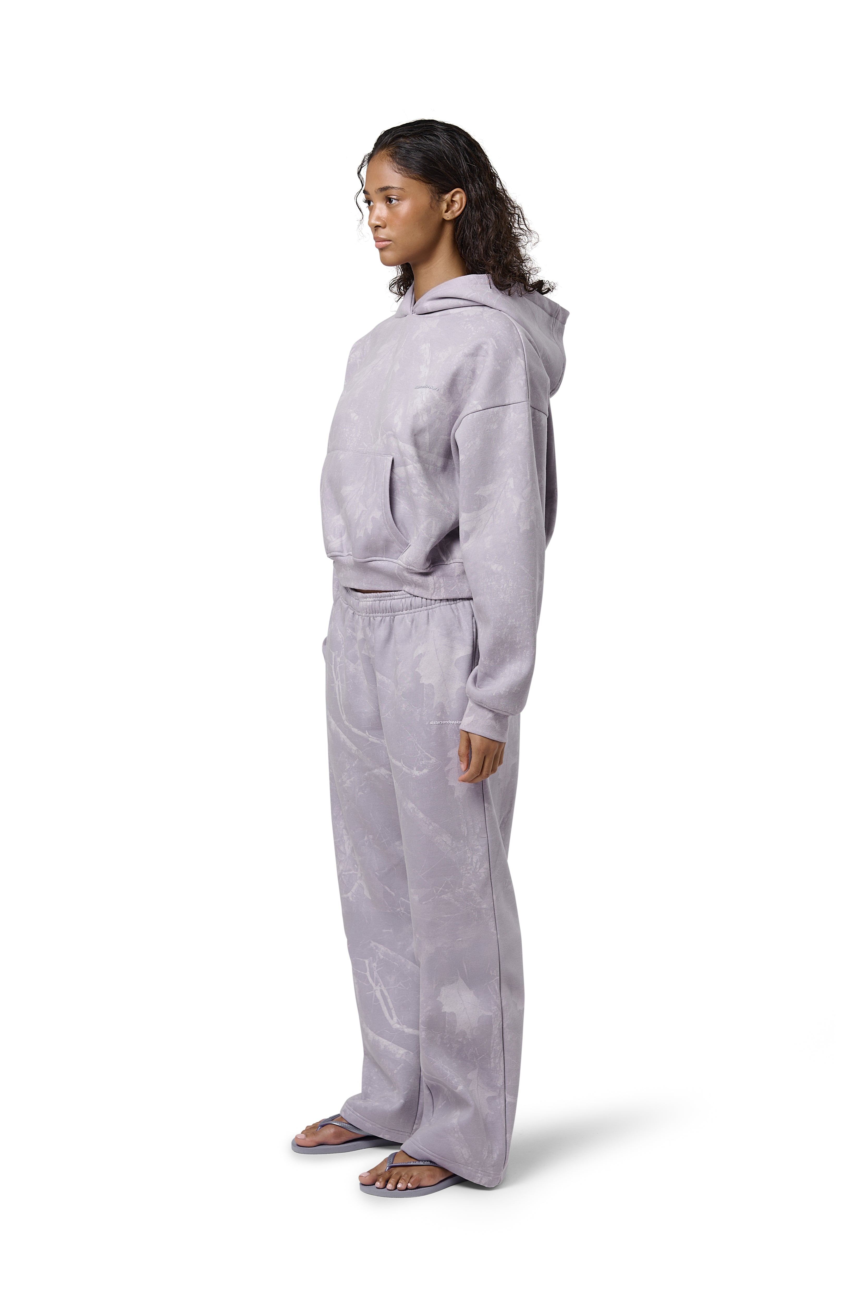 A lilac cropped hoodie with an all-over twig camouflage print, featuring a cropped relaxed fit, dropped shoulders, thick ribbed trims, and embroidered Sisters & Seekers logo.